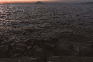 黃昏時分的岩石海岸，海浪和遠山在夕陽餘暉下