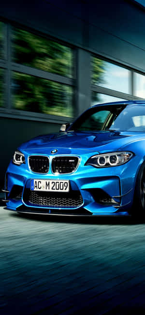 藍色BMW M2以動態模糊效果高速駛過現代建築。 — Realme 壁紙