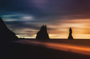 海蝕柱在沙灘上方的多彩日落天空中形成剪影。 — MacBook Air M3 壁紙