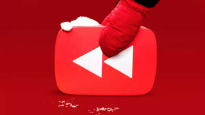 戴紅色手套的手拿著一個被雪覆蓋的YouTube播放按鈕。