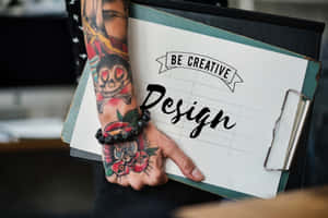 紋身的手拿著寫有「Be Creative Design」文字的寫字板。