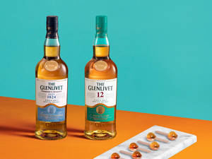 兩瓶Glenlivet威士忌搭配琥珀色石頭，放置在大理石板上，背景為藍綠色和橙色。