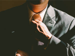 特寫一名男子在溫暖燈光下調整深色西裝中的領帶。