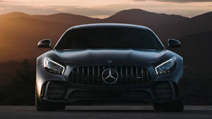 啞光黑色Mercedes-AMG GT在夕陽下對著鏡頭，背景有山脈。