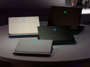 四部 Alienware 遊戲筆記型電腦，帶有發光標誌，在展示桌上。