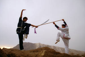 兩位武術家在黃昏時分的岩石山上練習劍和棍技巧。
