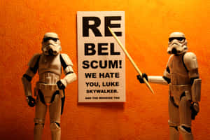 兩個風暴兵可動人偶站在一個橙色牆壁前，旁邊有一個寫著「Rebel Scum!」的標語牌。