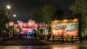 Cars Land 主題公園的夜間街道，有發光的標誌和一個大型歡迎牌。