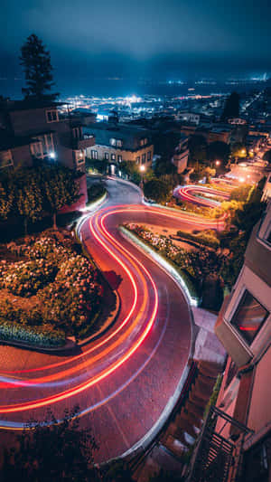 夜晚蜿蜒的城市街道，汽車的紅色光軌和盛開的花壇。