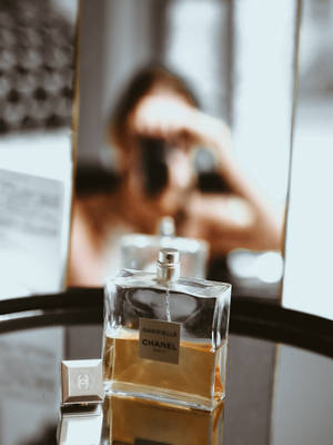 Chanel Gabrielle 香水瓶，背景有模糊人影拿著相機。