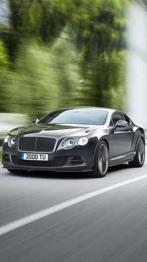 黑色賓利 Continental GT 在道路上奔馳，綠色樹木呈現動態模糊效果。