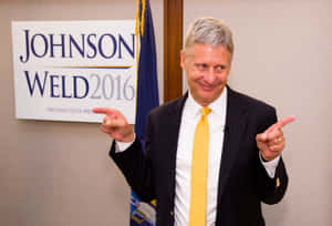 穿著西裝同黃色領帶嘅男人指向Johnson Weld 2016嘅競選標誌。
