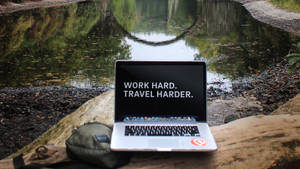 池塘旁圓木上的手提電腦，附有勵志名言 work hard travel harder
