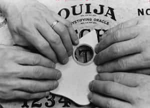 四隻手喺字母上面揸住 Ouija 板嘅指示器。