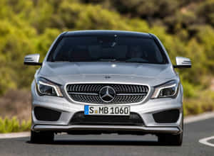 銀色 Mercedes-Benz CLA 在彎曲的道路上行駛，穿過綠樹叢。 — 銀色 壁紙