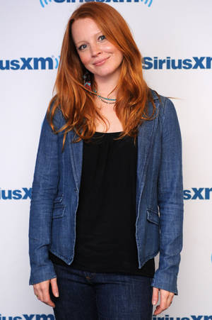 紅髮女性穿牛仔外套在SiriusXM活動中對鏡頭微笑。