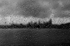 玻璃上的雨滴遮擋了灰色天空下模糊的城市天際線。