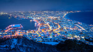 夜晚沿海灣的積雪城市燈光。 — 日本 壁紙