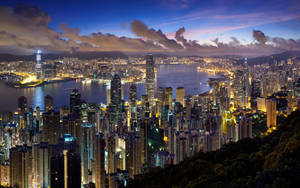 黃昏時分的香港天際線，燈火通明的建築物和港口水域