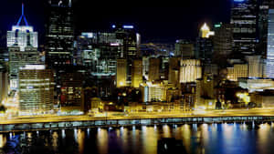 夜晚城市天際線，發光的建築物倒映在河流中。