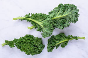 三塊新鮮的羽衣甘藍葉在白色大理石背景上。