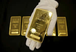 戴著白色手套的手拿著一塊1000g金條，背景有其他金條。 — 金色 壁紙