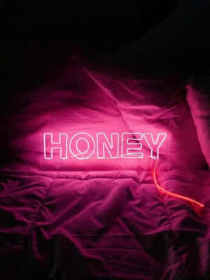在昏暗房間的深色床罩上，一個寫著honey的粉紅色霓虹燈牌。