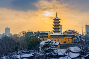 夕陽下被雪覆蓋的金色寶塔寺廟，背後有現代城市天際線。 — 唐人街 GIF 壁紙