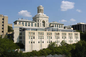 一座米色建築，帶有塔樓和拱形窗戶，在藍天下被綠樹環繞。