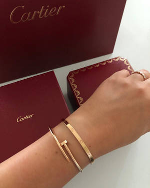 手戴Cartier金色手鐲和戒指，附近有品牌盒子。
