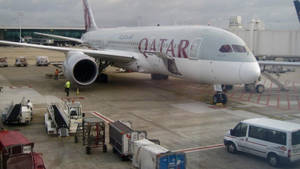 卡塔爾航空飛機在機場閘口，有地勤人員和服務車輛。