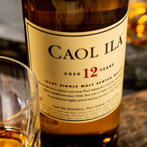 Caol Ila 12年威士忌酒瓶和玻璃杯放在木桌上。