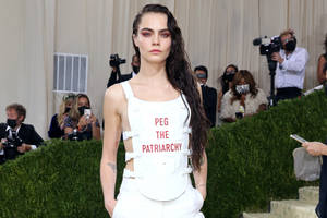 模特兒Cara Delevingne在紅地毯活動中穿著白色服裝，上有紅色文字「PEG THE PATRIARCHY」。