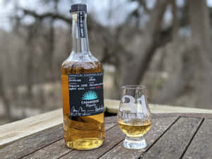 一瓶Casamigos tequila和一個品牌玻璃杯放在戶外的木桌上。