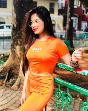 身穿橙色服裝的女性在城市公園中倚靠綠色欄杆
