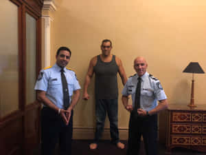 兩名警察站在一個穿著背心的肌肉男兩側，室內。