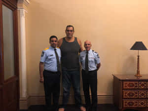 兩名警員在室內站在一名穿背心的高大男子兩側。