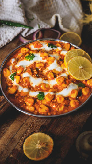 一碗chole masala，配上檸檬片和芫荽，放在木桌上。