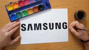 人在白紙上用水彩畫Samsung標誌。