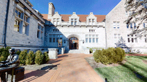 石造大學建築，有雕像和磚砌步道，在明亮陽光下。