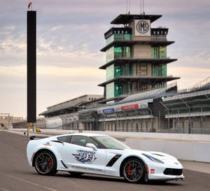 白色Corvette Indy 500 Pace Car在賽道上，背景有IMS塔和日落。 — 酷車 壁紙