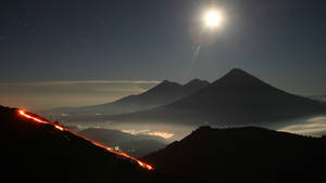 夜晚噴發的火山，發光的熔岩流和上方明亮的月亮。