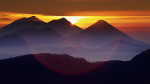 夕陽映照山峰，帶有大氣薄霧和鏡頭光暈。 — 美麗的日落動畫 壁紙