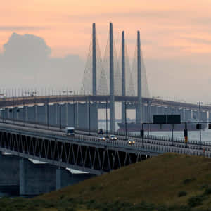 汽車在日落時分駛過一座大橋，水面上有一艘貨船。