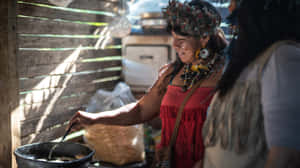 身穿紅色連衣裙和羽毛頭飾的原住民女性在木棚裡做飯。