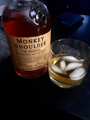 Monkey Shoulder威士忌酒瓶和加冰酒杯放在深色桌子上。