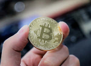 手拿著一枚帶有電路設計的金色比特幣硬幣。 — 比特幣 壁紙