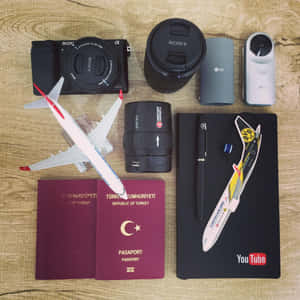 旅行裝備包括護照、相機鏡頭和YouTube筆記本，置於木質表面。 — iPad Pro 13 壁紙