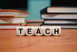 拼出 TEACH 的木製積木放在書桌上，背景有書堆。