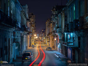 夜晚街道，舊建築之間有移動汽車的紅色光跡。
